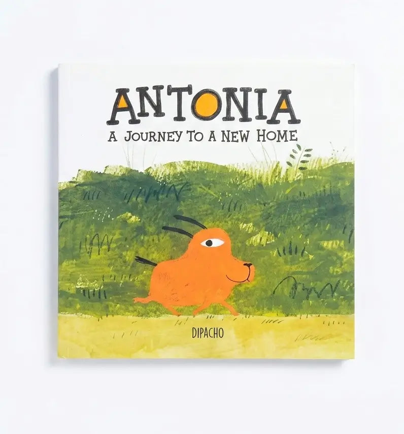 A children's book cover titled 'ANTONIA A JOURNEY TO A NEW HOME' with an orange goat-like character walking through green grass on a yellow ground, shown against a light gray background.