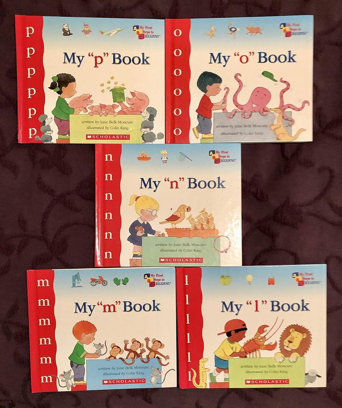 Set of five children's books titled 'My 'p' Book', 'My 'o' Book', 'My 'n' Book', 'My 'm' Book', and 'My 'l' Book' on a dark textured background.
