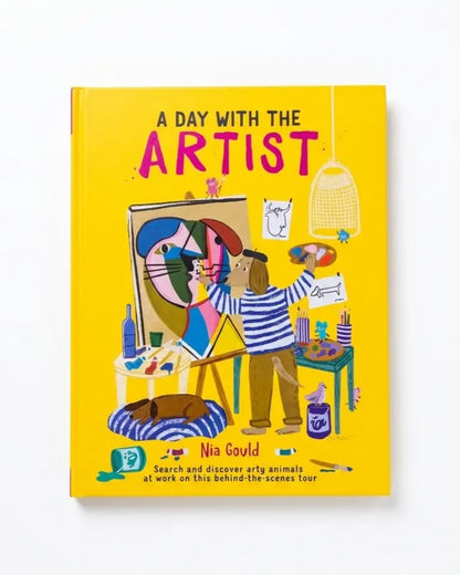 A hardcover children's book titled 'A Day With the Artist' by Nia Gould, featuring a bright yellow cover with a colorful cartoon illustration of an artist painting a cat.