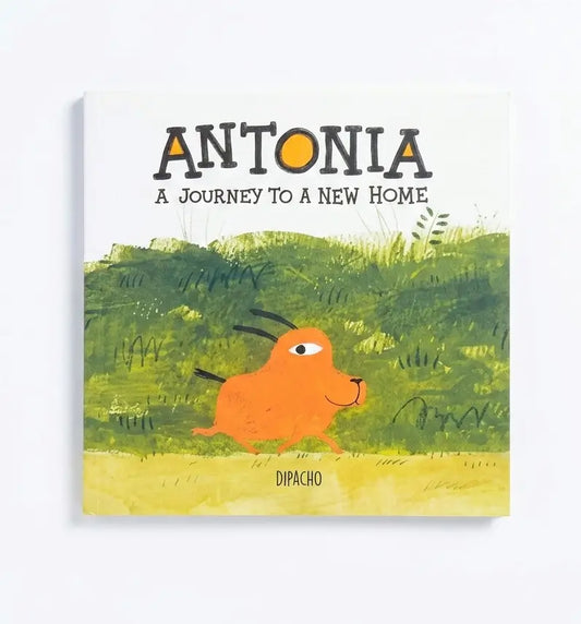 A children's book cover titled 'ANTONIA A JOURNEY TO A NEW HOME' with an orange goat-like character walking through green grass on a yellow ground, shown against a light gray background.
