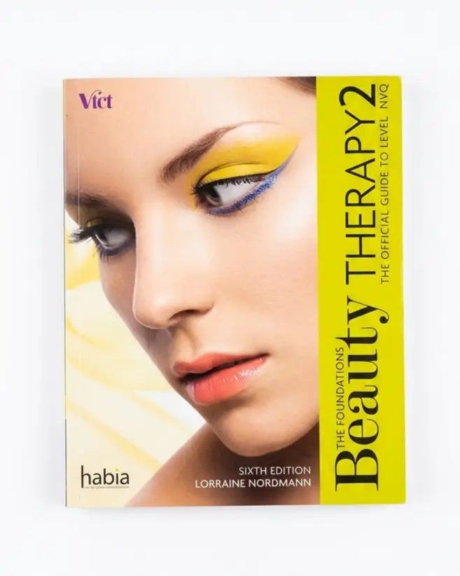 The Foundations' Beauty Therapy 2 Sixth Edition NQO Level 1 QRO by Lorraine Nordmann, published by habia and Victor. The book cover features a close-up of a model's face with dramatic yellow and blue eyeshadow, set against a bright yellow and white background.