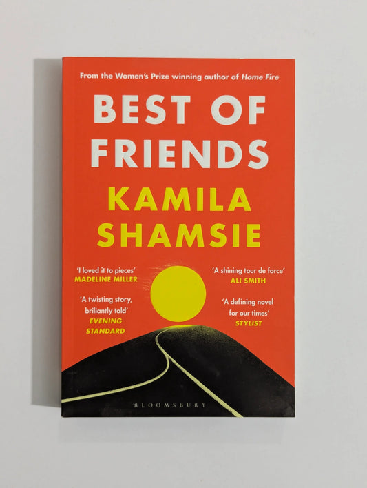 The book cover of 'Best of Friends' by Kamila Shamsie, featuring a bold orange-red background with large white and yellow title text, a yellow circle graphic, and a black road illustration at the bottom. The Bloomsbury publisher name is visible at the bottom.