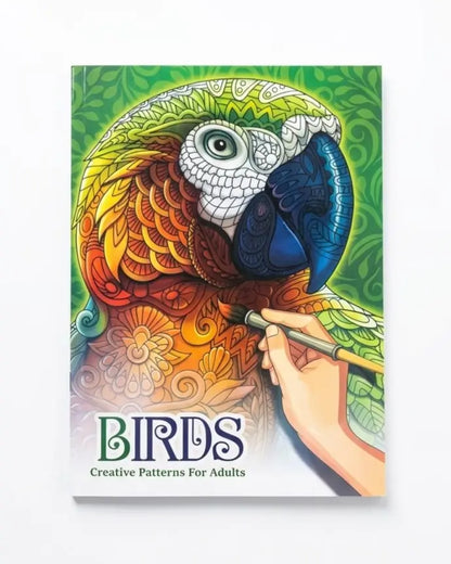 Adult coloring book titled 'BIRDS: Creative Patterns For Adults' featuring a highly detailed, colorful illustration of a parrot being painted by a hand, set against a clean white background.