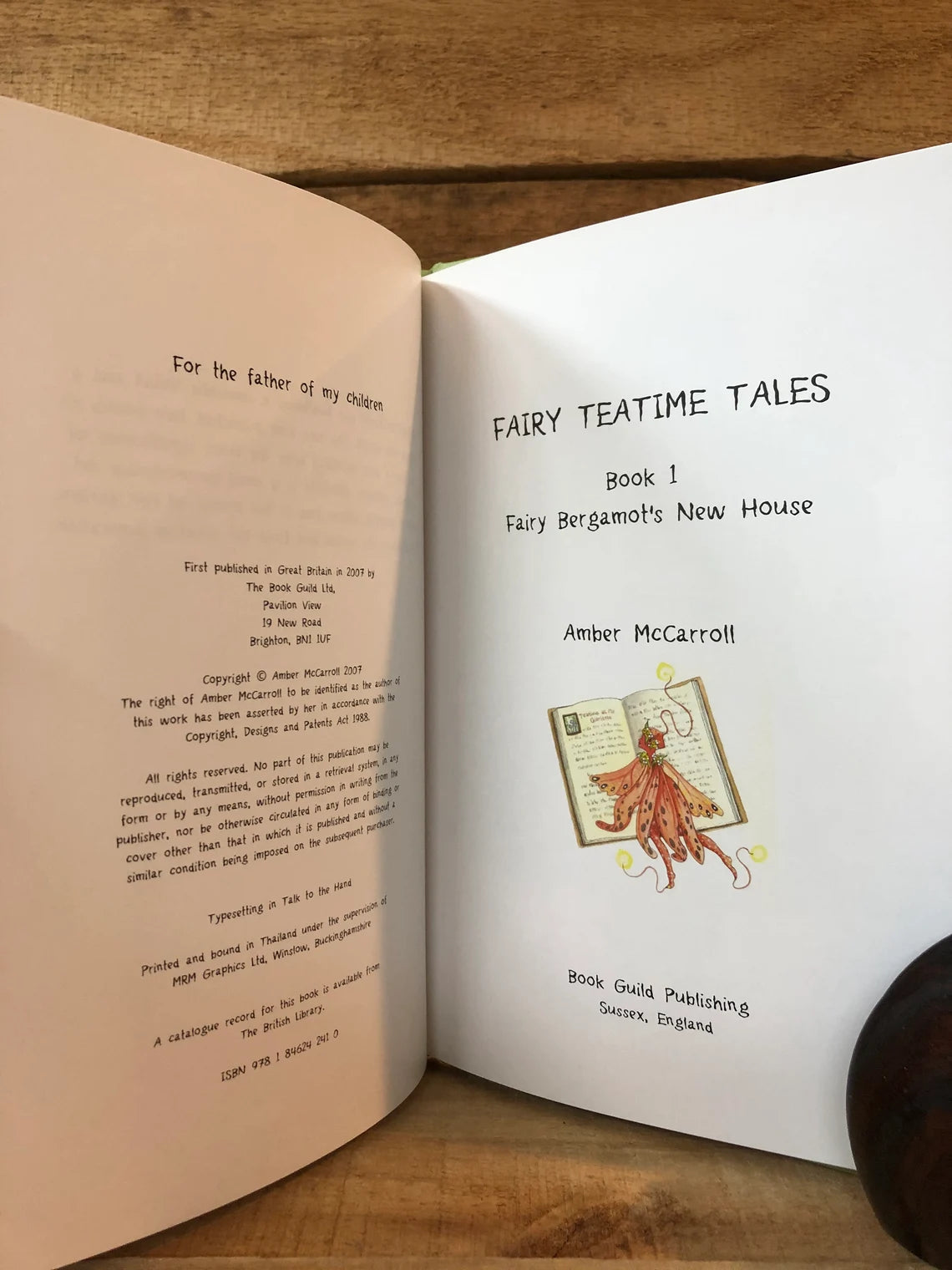 Open book with 'Fairy Teatime Tales' title and illustration on a wooden surface