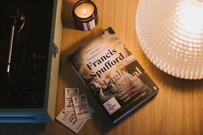 Book titled 'High Contrast' by Francis Spufford on a wooden surface with a candle and lamp.