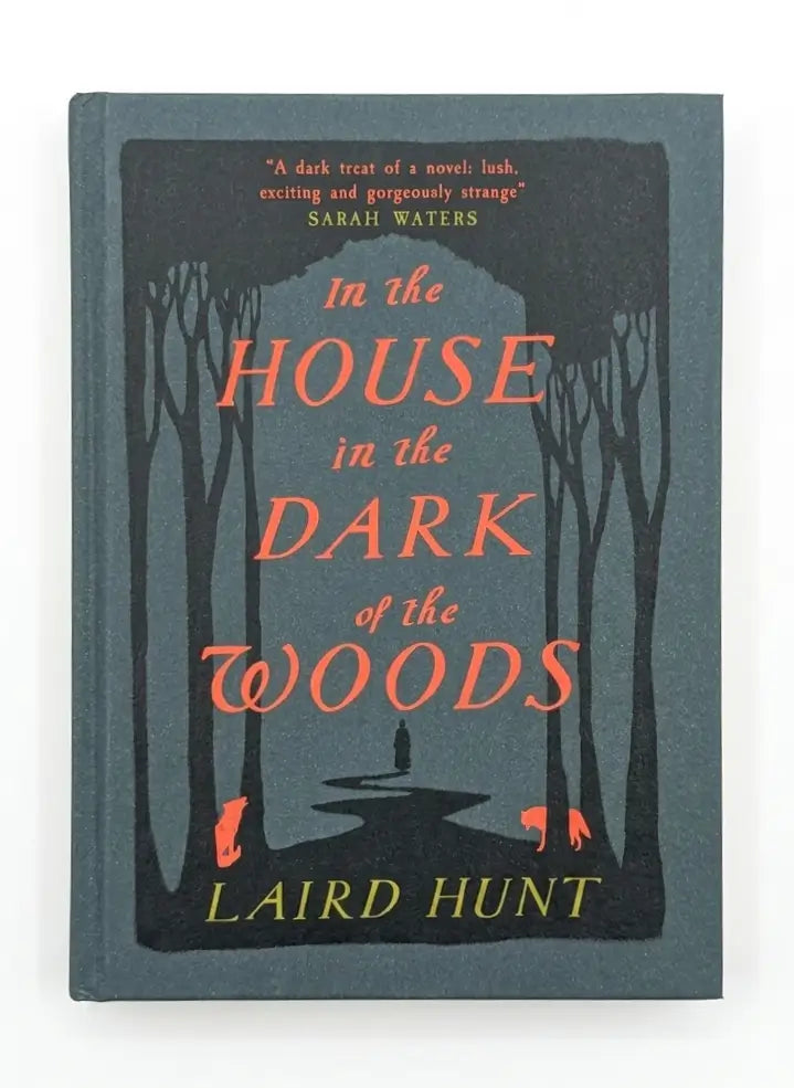 The book cover of 'In the House in the Dark of the Woods' by Laird Hunt, featuring a dark forest illustration with silhouetted trees and a path, with the title in coral-red and the author's name in yellow on a muted blue-gray background.