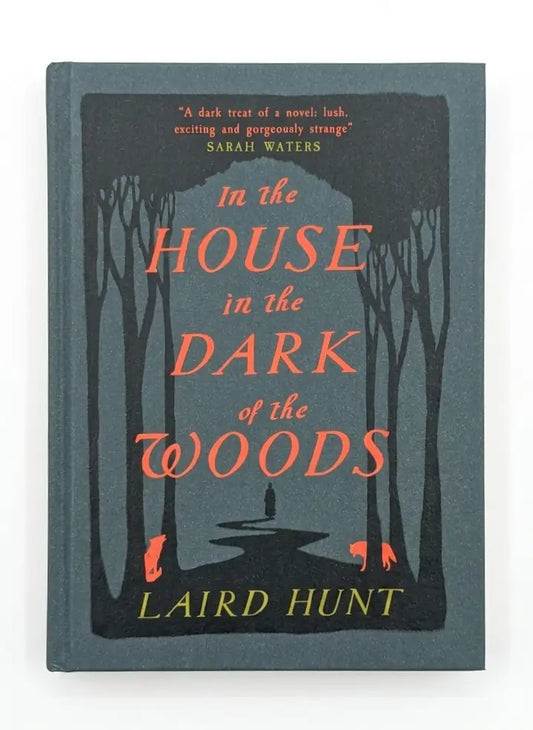 The book cover of 'In the House in the Dark of the Woods' by Laird Hunt, featuring a dark forest illustration with silhouetted trees and a path, with the title in coral-red and the author's name in yellow on a muted blue-gray background.