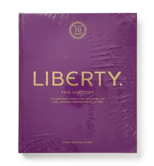 A hardcover book titled "LIBERTY. THE HISTORY" wrapped in clear plastic, featuring a solid purple cover with gold lettering and a small gold circular emblem near the top.