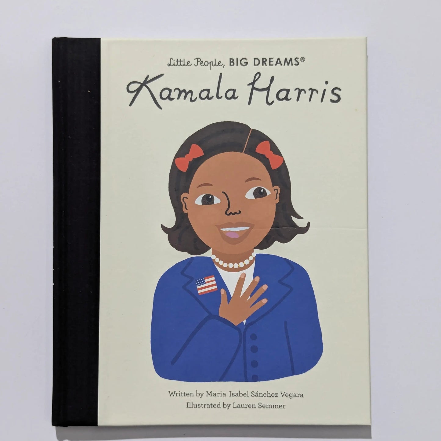 A children's book titled 'Little People, BIG DREAMS Kamala Harris' with a cream-colored cover, black spine, and an illustrated portrait of Kamala Harris wearing a blue blazer and red hair bows.