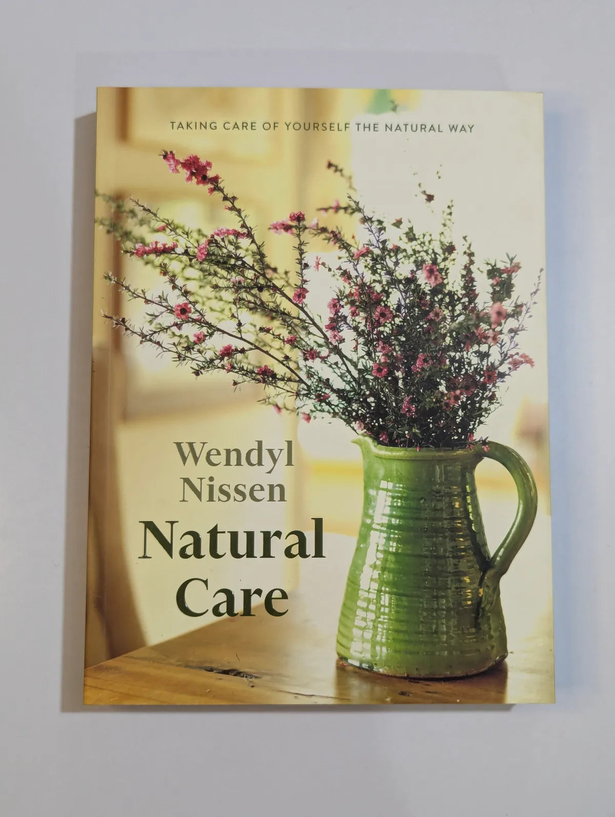 Book cover of 'Natural Care' by Wendyl Nissen with a green pitcher and flowers on a wooden surface.