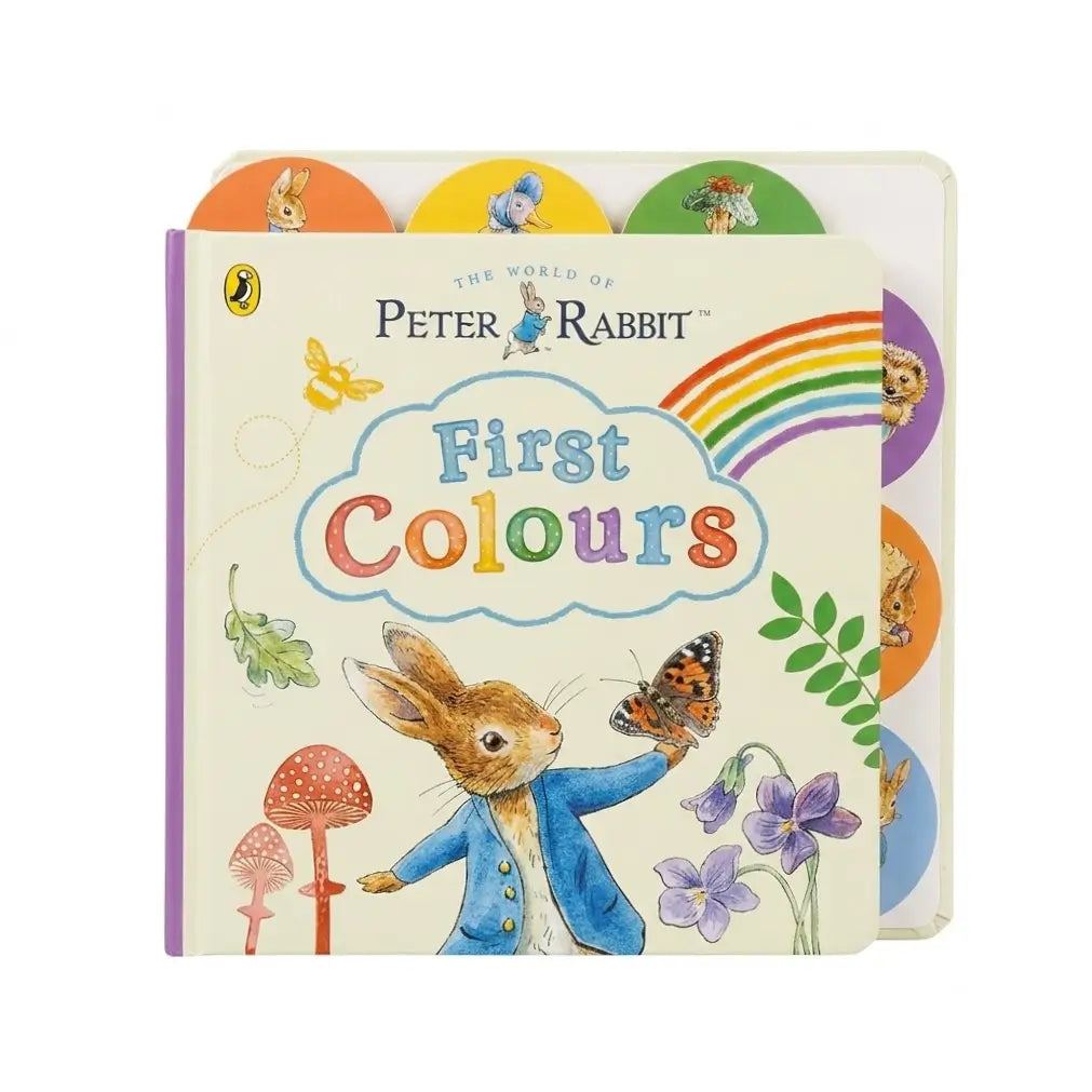 A children's hardcover book titled 'First Colours' from 'The World of Peter Rabbit' by Puffin, featuring a cream cover with colorful illustrations of Peter Rabbit, flowers, mushrooms, a butterfly, and a rainbow, with circular color tabs peeking out from the back.
