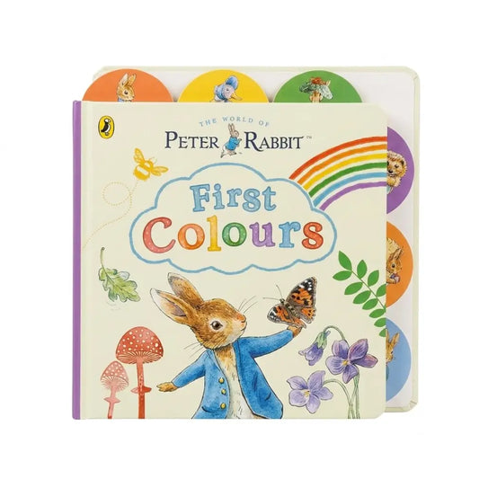 A children's hardcover book titled 'First Colours' from 'The World of Peter Rabbit' by Puffin, featuring a cream cover with colorful illustrations of Peter Rabbit, flowers, mushrooms, a butterfly, and a rainbow, with circular color tabs peeking out from the back.