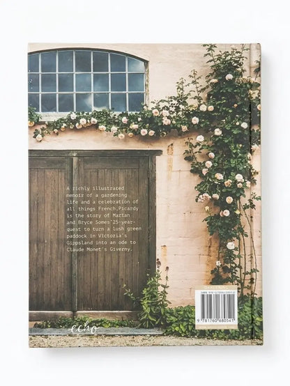 A hardcover book standing upright against a white background, showing the back cover with a photograph of a rustic beige wall, dark wooden door, window, and climbing white flowers. The title and subtitle text are printed on the cover, along with a barcode and small logo near the bottom.