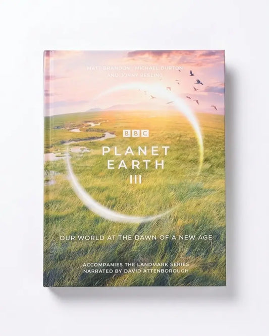 The book cover of 'Planet Earth III' is shown standing upright against a clean white background. The cover features a scenic landscape of a green valley under a warm sunset sky with birds flying, overlaid with a large white circular graphic and the BBC logo and title text.