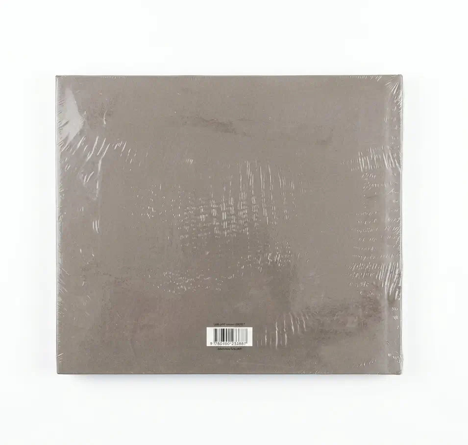 A square, shrink-wrapped album or book-style package in a muted taupe-gray color, photographed against a plain white background.