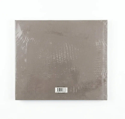 A square, shrink-wrapped album or book-style package in a muted taupe-gray color, photographed against a plain white background.