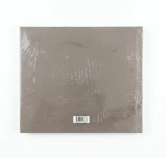 A square, shrink-wrapped album or book-style package in a muted taupe-gray color, photographed against a plain white background.