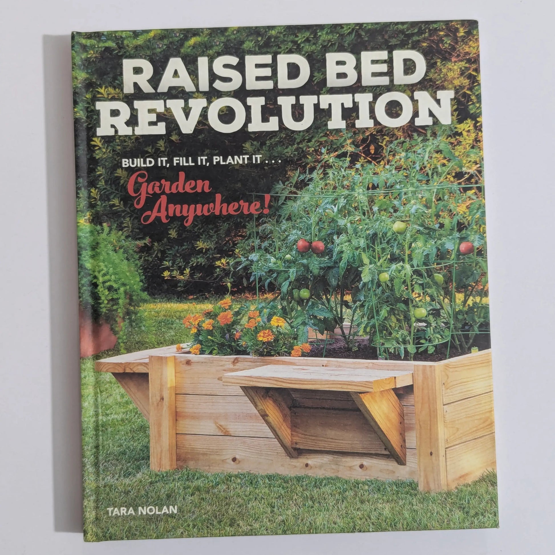 The front cover of the book 'Raised Bed Revolution' by Tara Nolan, featuring a wooden raised bed garden planter in a lush green garden setting. The title is displayed in large white letters at the top, with the subtitle 'Build It, Fill It, Plant It.
