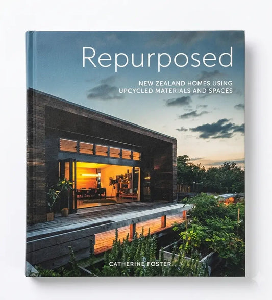 The book cover of 'Repurposed: New Zealand Homes Using Upcycled Materials and Spaces' by Catherine Foster, featuring a modern house with large glass windows and warm interior lighting under a sunset sky.