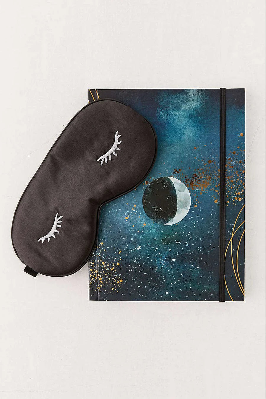 Black sleep mask and notebook with celestial design on a white background