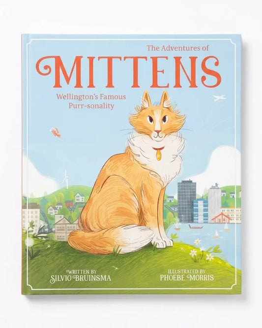 The Adventures of Mittens children's book cover, featuring an illustration of an orange and white cat named Mittens sitting on a grassy hill with Wellington cityscape in the background. The title 'MITTENS' is written in large orange letters at the top.
