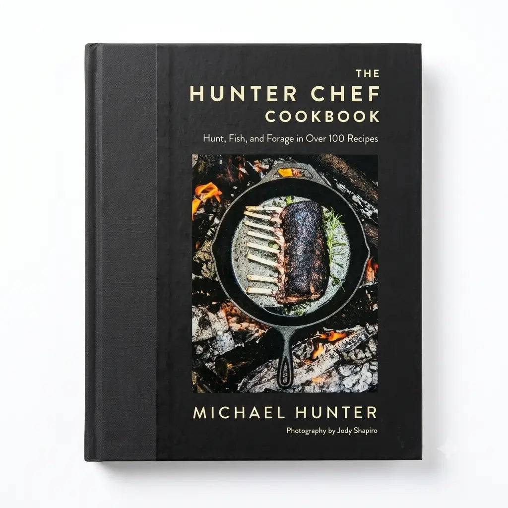 The Hunter Chef Cookbook by Michael Hunter, a hardcover book with a black cover and gold lettering, featuring a central image of ribs cooking in a cast iron skillet over embers.
