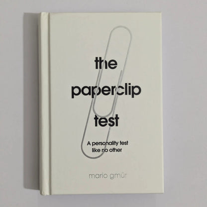 A hardcover book titled 'the paperclip test' by Mario GMUR, featuring a minimalist cream cover with a large black paperclip graphic and black text, photographed against a neutral gray background.
