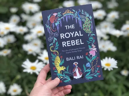 Book titled 'The Royal Rebel' held in front of white flowers