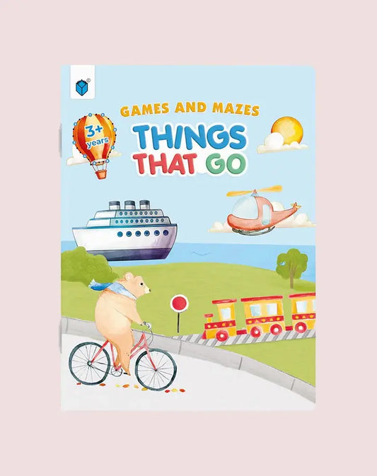 Children's activity book cover titled 'Games and Mazes Things That Go' featuring a playful illustrated scene with a pig riding a bicycle, a hot air balloon, a cruise ship, a helicopter, and a train on a light pink background.