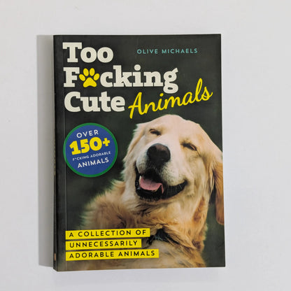 The book 'Too F*cking Cute Animals' by Olive Michaels, featuring a golden retriever on the cover, photographed standing upright against a plain white wall.