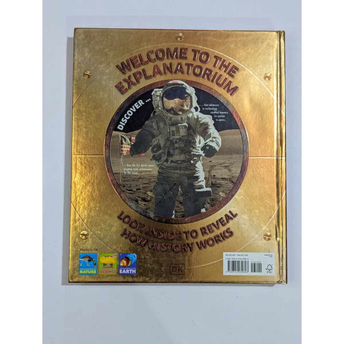 Gold book cover with astronaut illustration and text 'Welcome to the Explanatorium' on a white background